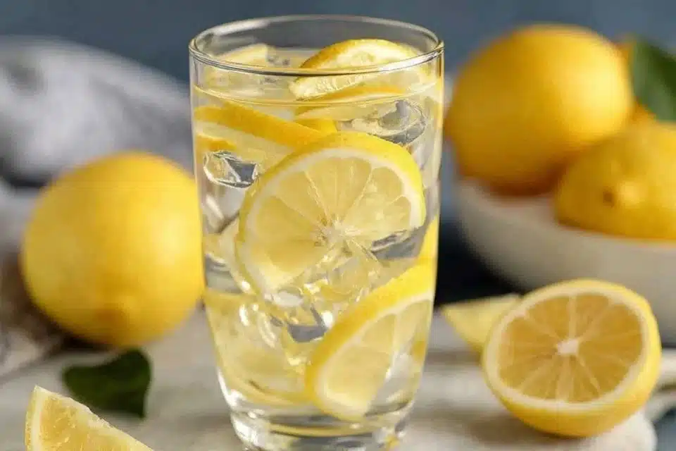 Lemon Water 3 A glass of lemon water with lemon slices and mint leaves on a wooden table.
