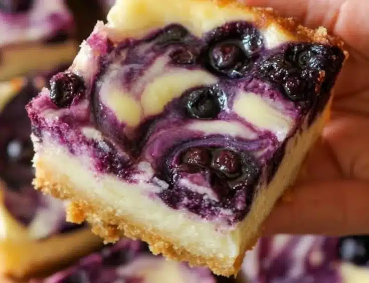 Blueberry ripple cheesecake bars on a plate with fresh blueberries